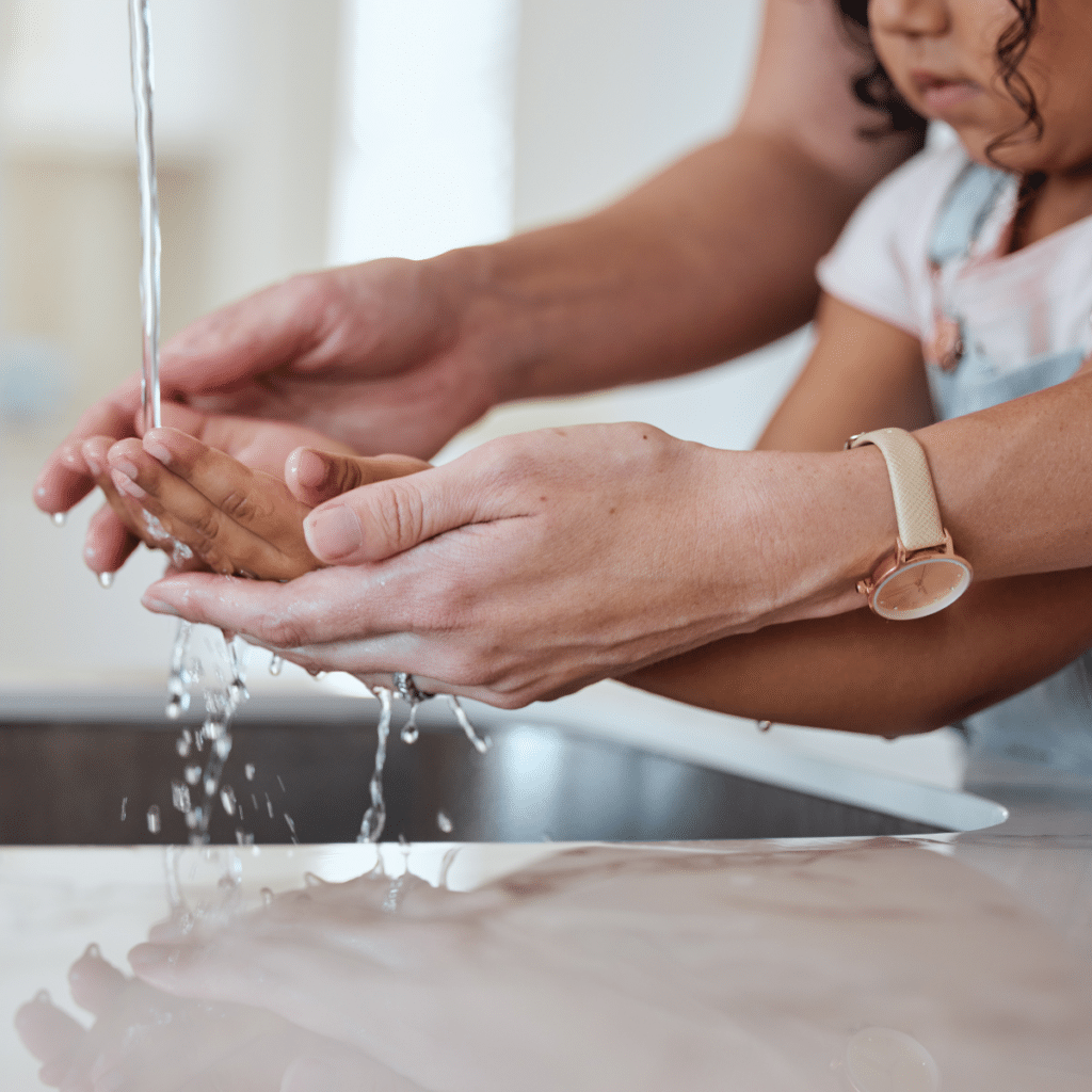 An adult helping a child wash hands under a running faucet