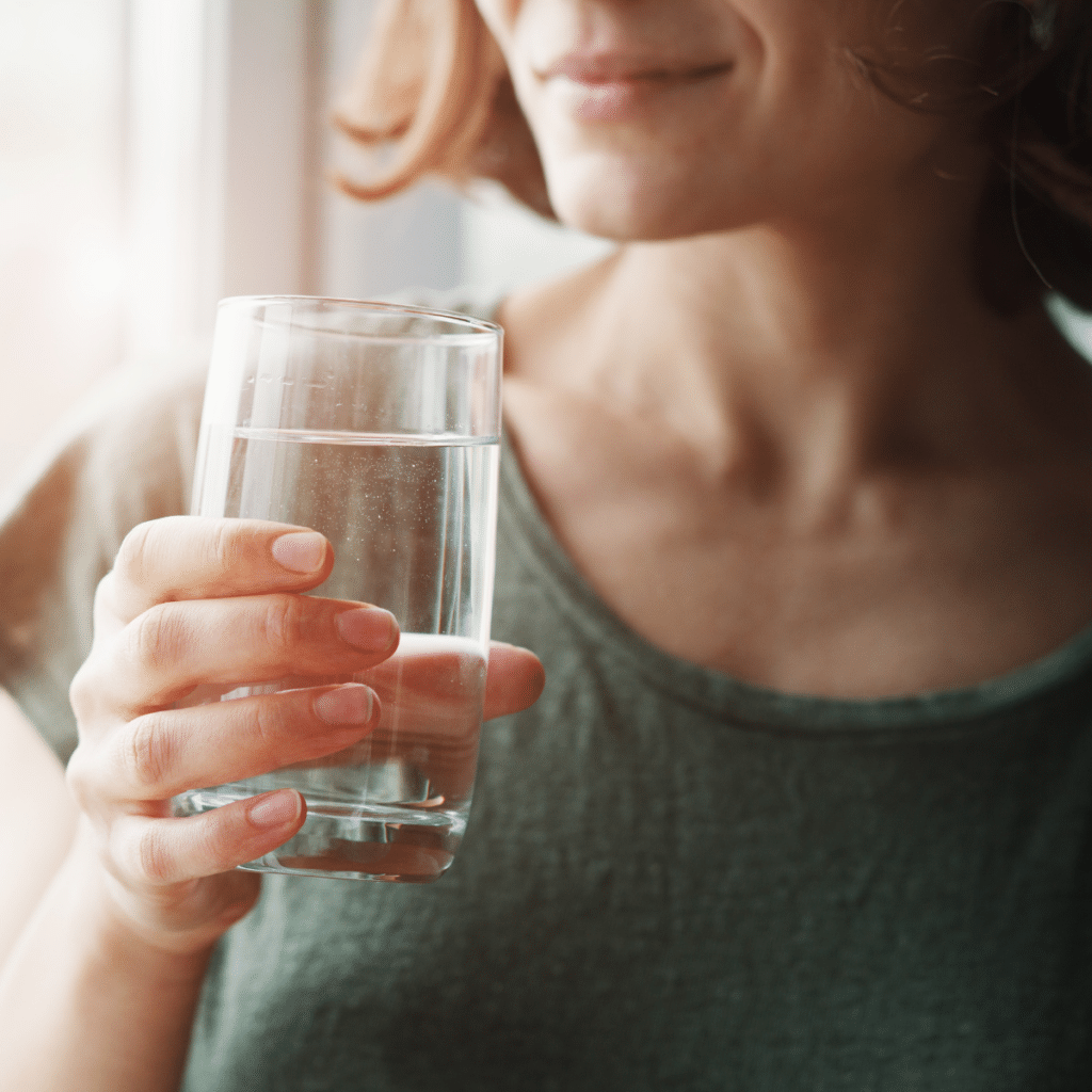 A woman holding a glass of water near a window with soft lighting