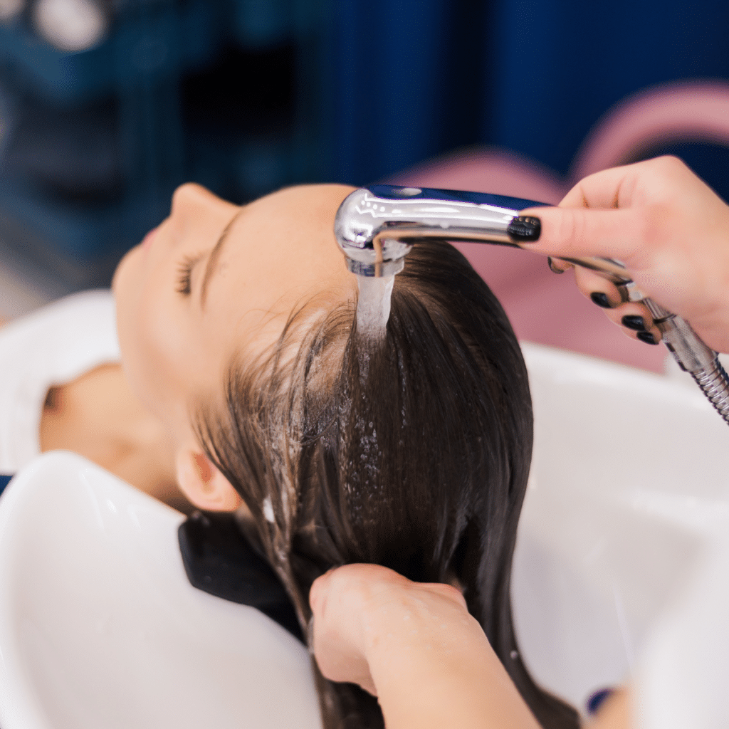 A hairstylist washing a client's hair with a handheld sink sprayer