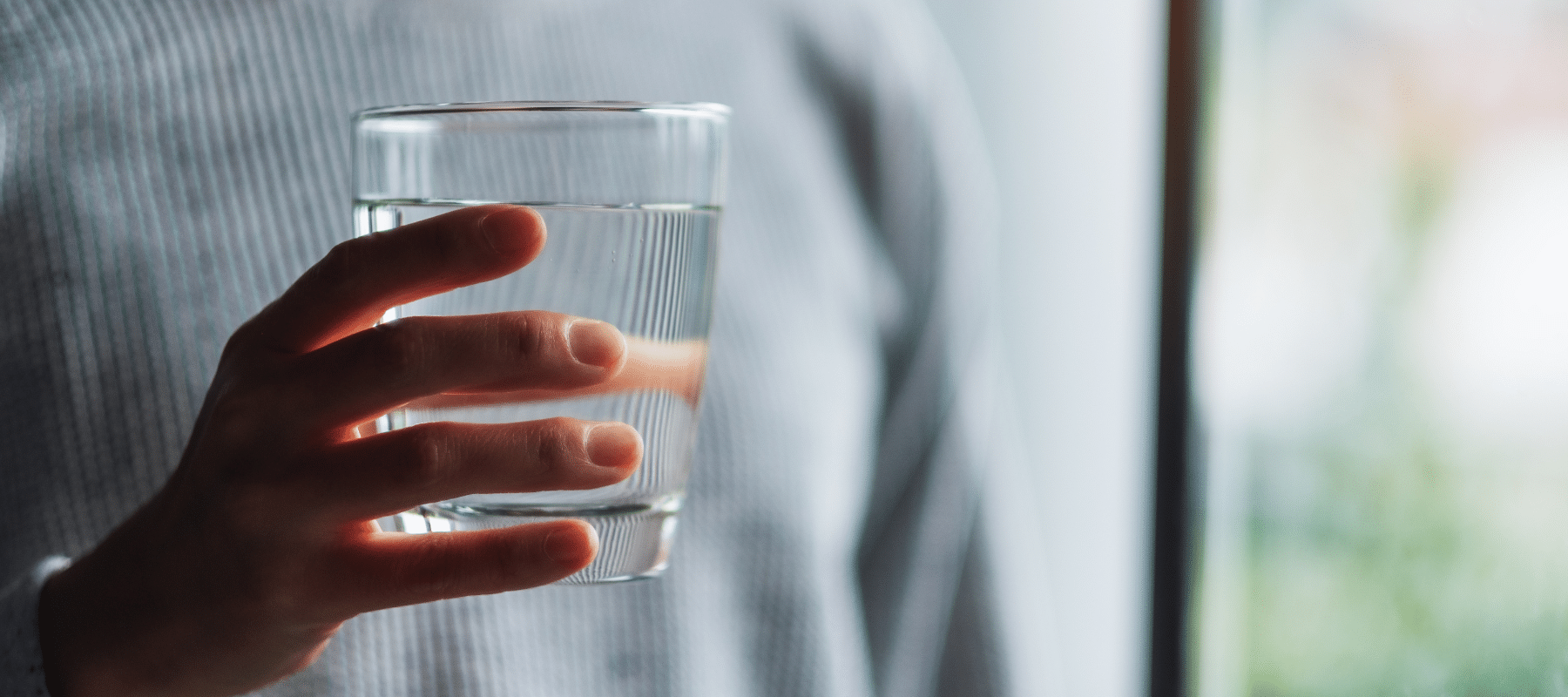 A person holding a glass of clear water near a window