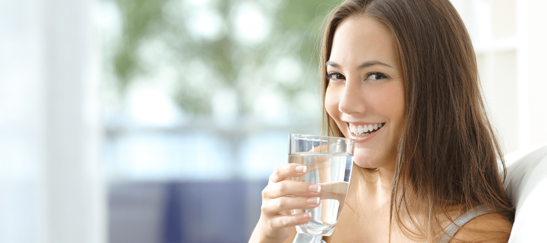 A woman with long brown hair smiling while holding a glass of water