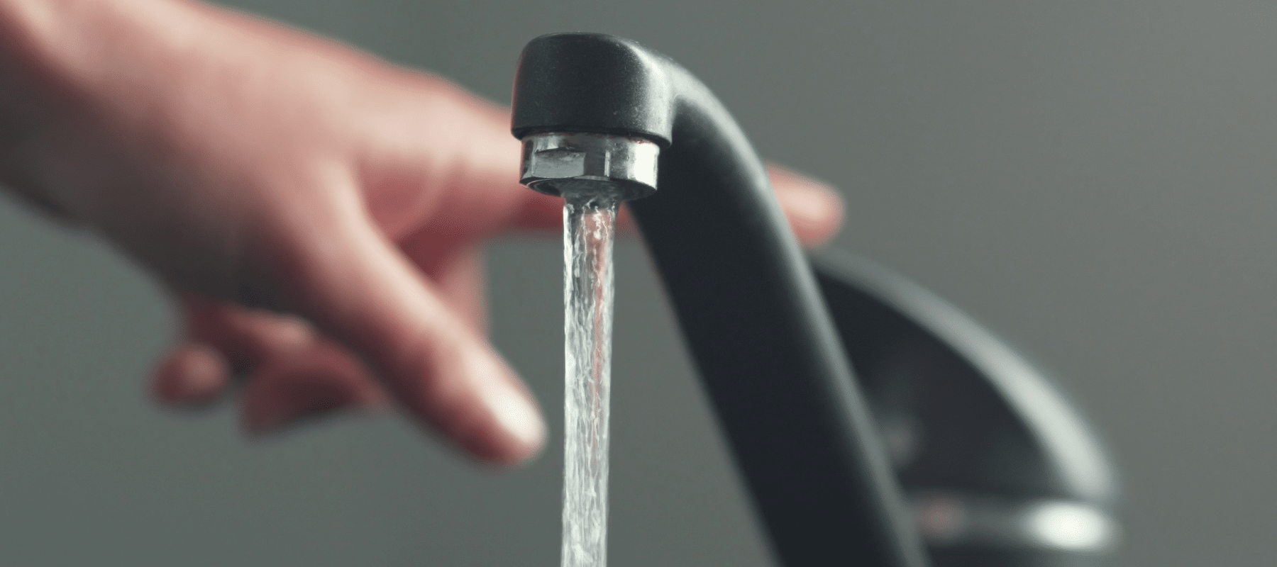 A close-up of a hand reaching for a running kitchen faucet