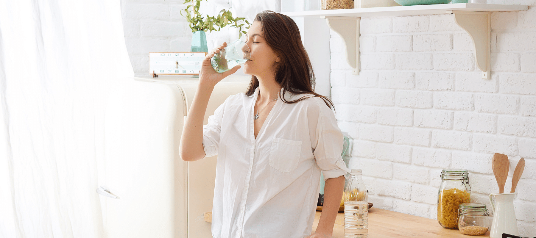 A woman drinking water in a bright kitchen with natural light