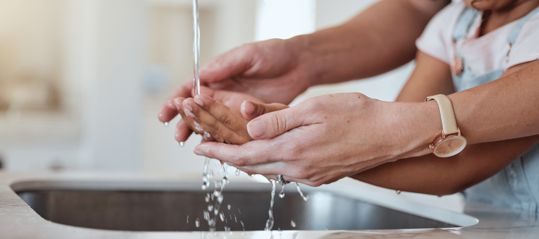 An adult helping a child wash hands under a running faucet